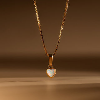 Opal Herz Kette in Gold: Opal in Herzform an feiner Box Chain vor warmem Hintergrund