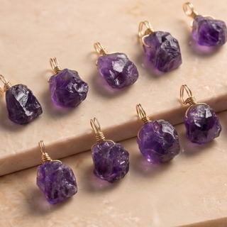 Zehn lila Amethyst Rohsteine auf beigem Marmor, jeder in eigener Form