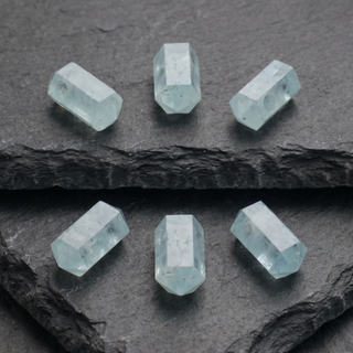 Sechs Aquamarin Zylinder in Pastellblau auf schwarzem Stein verteilt