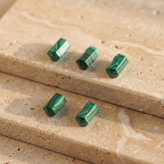 Six green malachite cylinders with gold bails on beige natural stone