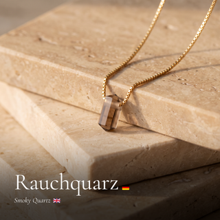Rauchquarz Zylinderanhänger an Goldkette auf Travertin mit Schriftzug Rauchquarz