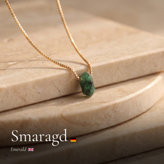 Smaragd Zylinderanhänger an Goldkette auf Travertin mit Schriftzug Smaragd