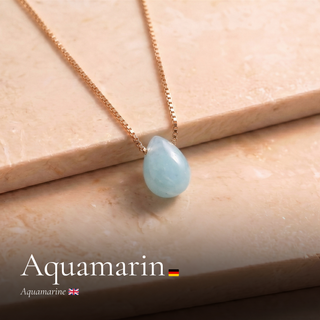 Aquamarin Tropfen an Goldkette auf Travertin mit Schriftzug Aquamarin