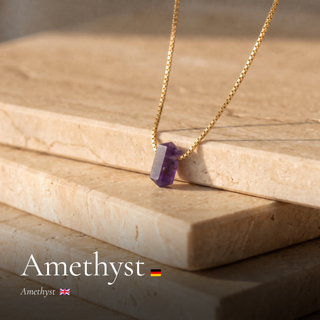 Amethyst Zylinderanhänger an Goldkette auf Travertinkante mit Schriftzug Amethyst