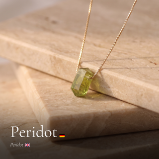 Peridot Zylinderanhänger an Goldkette auf Travertin mit Schriftzug Peridot