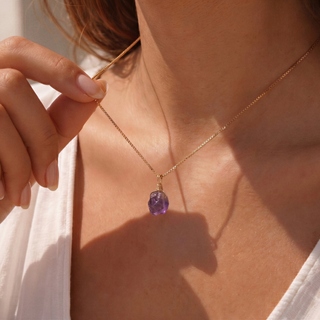Frau hält den kleinen rohen Amethyst an der Kette vor weißer Bluse