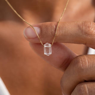 Frau zieht den transparenten Bergkristall Zylinder an der Goldkette nach vorn