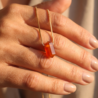 Karneol Zylinder auf dem Handrücken, feine Goldkette zwischen den Fingern