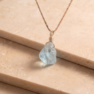Close-up of the raw aquamarine on a gold chain on light travertine