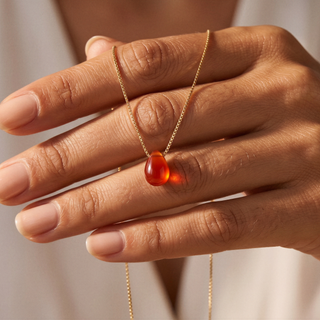 Karneol Tropfen auf den Fingern liegend, Goldkette über die Hand