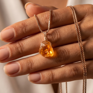 Raw citrine between the fingers with a gold chain over the hand