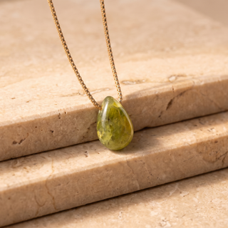 Peridot teardrop on a gold chain on a travertine step in side light