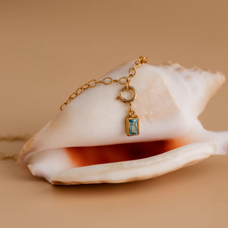 Detail: Der Aquamarin hängt mit einem Federring am goldenen Armband, darunter eine Meeresschnecke