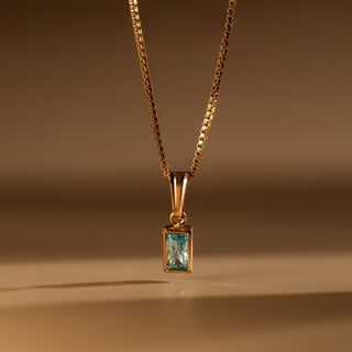 Aquamarin Kette in Gold: rechteckig facettierter Aquamarin an feiner Box Chain vor warmem Hintergrund