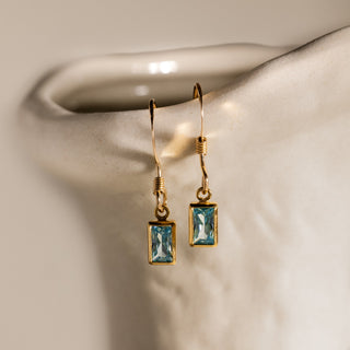 Aquamarin Ohrringe hängend in Gold: zwei facettierte Aquamarine an Ohrhaken vor heller Keramik