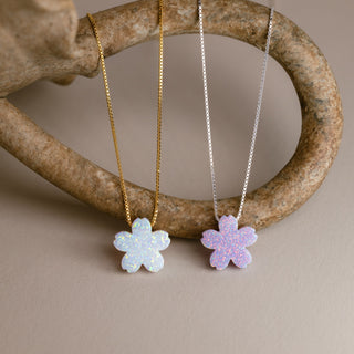 Flower necklace in gold with a white blossom and in silver with a lilac blossom on a curved ring