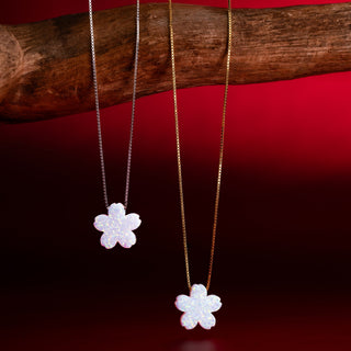 Two flower necklaces with white blossoms in silver and gold on a branch against a red background