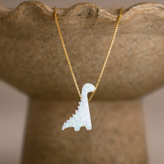 Synthetic Opal Dinosaur Necklace in gold with a white long-necked dinosaur on a stone-colored bowl