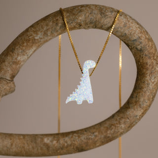 Gold dinosaur necklace with a white dinosaur on a curved stone-colored ring