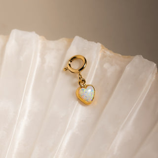 Opal Herz Charm in Gold: Opalherz mit Federring auf einer hellen Muschel