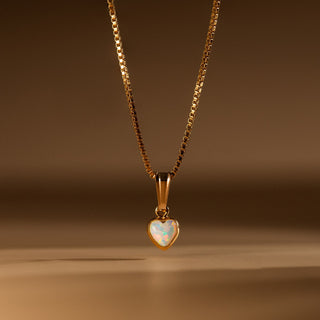 Opal Herz Kette in Gold: Opal in Herzform an feiner Box Chain vor warmem Hintergrund