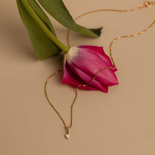 Lange goldene Kette mit Opalherz neben einer pinken Tulpe
