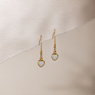 Opal heart drop earrings hanging from the edge of a sheet of paper