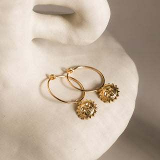 Creolen mit Anhänger in Gold auf einer hellen Keramikskulptur