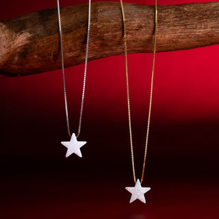 Zwei Sternketten mit weißem Stern in Silber und in Gold an einem Ast vor rotem Hintergrund